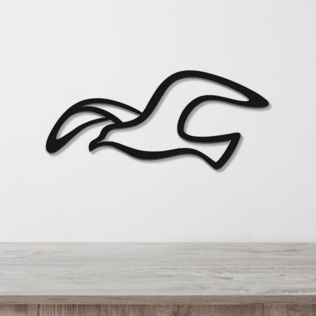 Black metal seagull wall art with flowing wing cutouts, mounted on a white wall above a light wood surface.