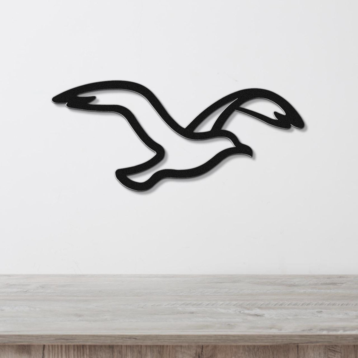 Black metal seagull wall art with a silhouette cutout design, mounted on a white wall above a light wood surface.
