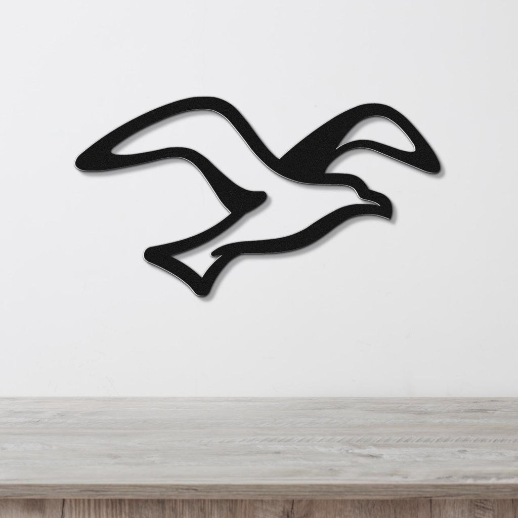 Black metal seagull wall art with flowing wing cutouts, mounted on a white wall above a light wood counter.