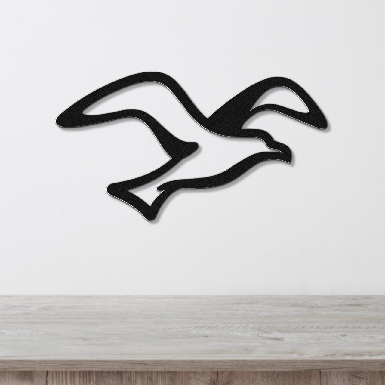 Black metal seagull wall art with flowing wing cutouts, mounted on a white wall above a light wood counter.