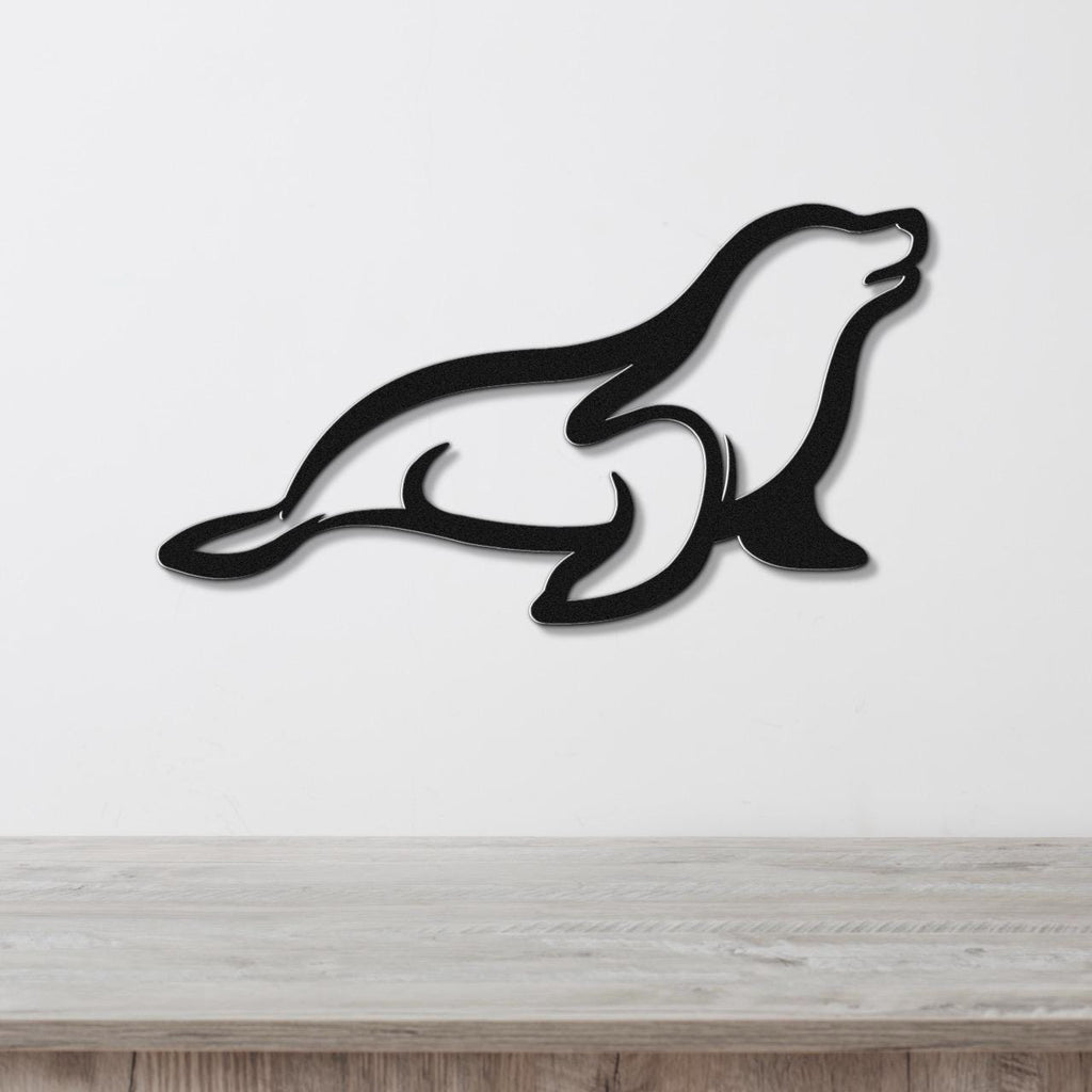 Black metal sea lion wall art with a sleek silhouette design, mounted on a white wall above a light wood surface.