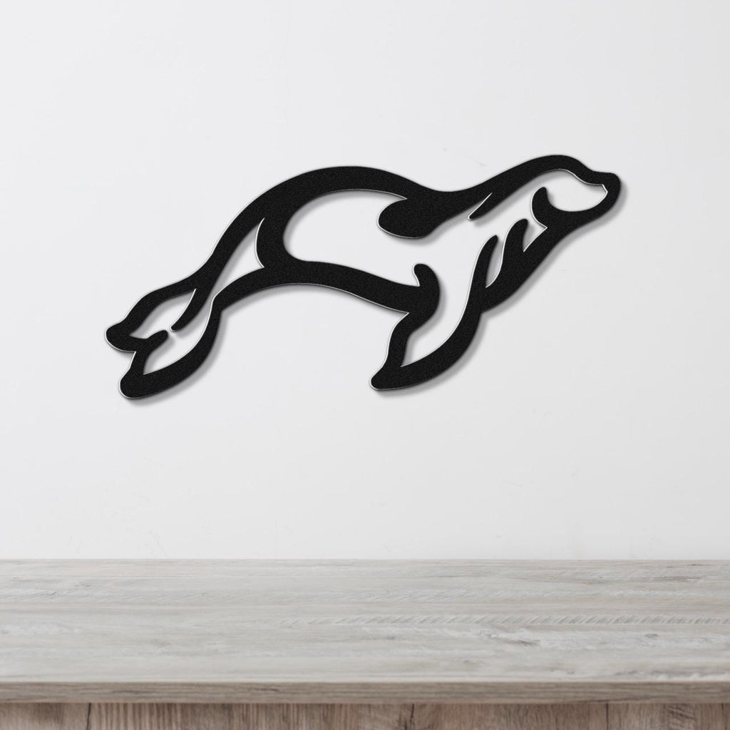 Black metal wall art in the silhouette of a leaping sea lion, mounted on a white wall above a light wood surface.