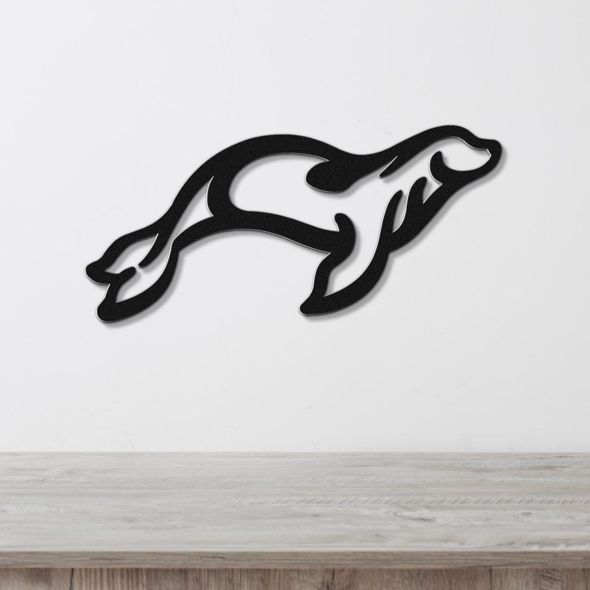 Black metal wall art in the silhouette of a leaping sea lion, mounted on a white wall above a light wood surface.