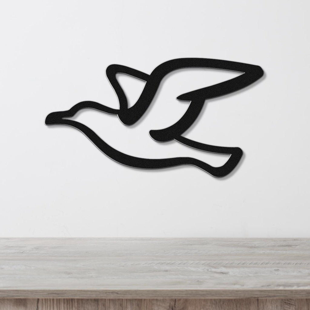 Black metal seagull wall art with a cutout silhouette design, mounted on a white wall above a light wood surface.