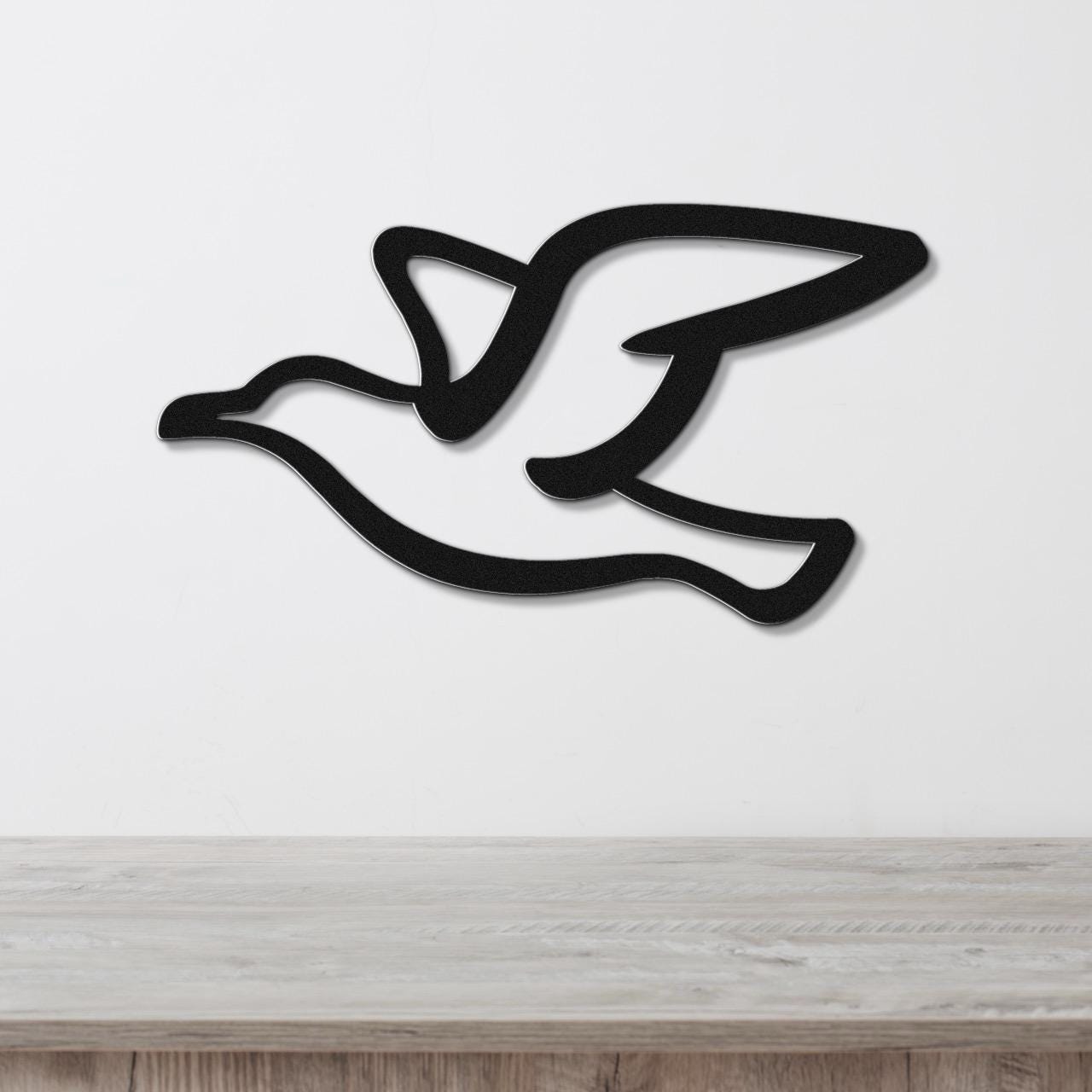 Black metal seagull wall art with a cutout silhouette design, mounted on a white wall above a light wood surface.