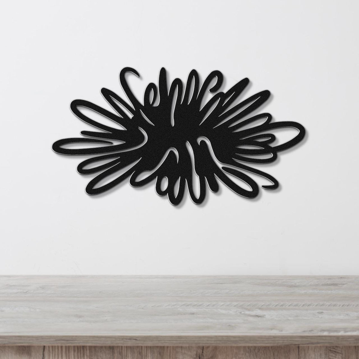 Black metal sea urchin wall art with spiky, radiating cutouts, mounted on a white wall above a light wood surface.