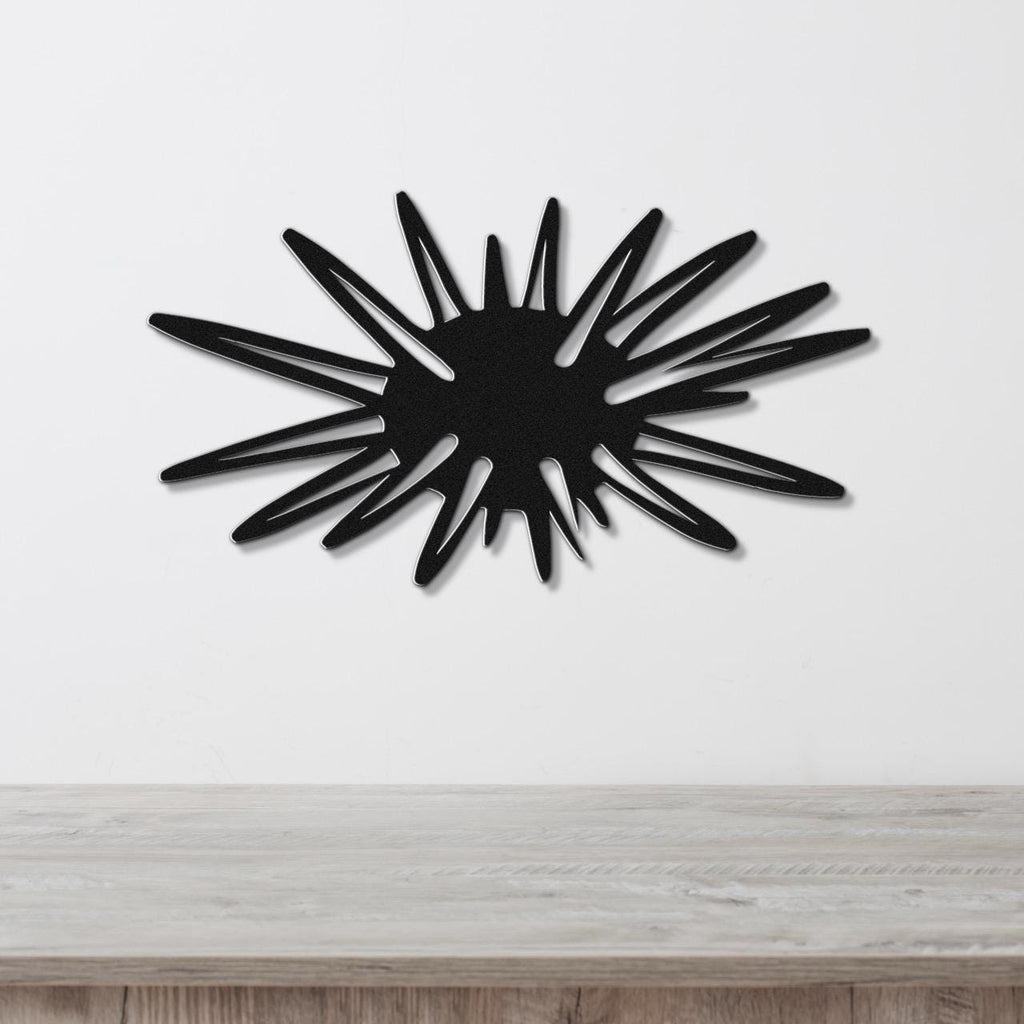 Black metal wall art in a sea urchin silhouette with radiating spines, mounted on a white wall above a light wood surface.