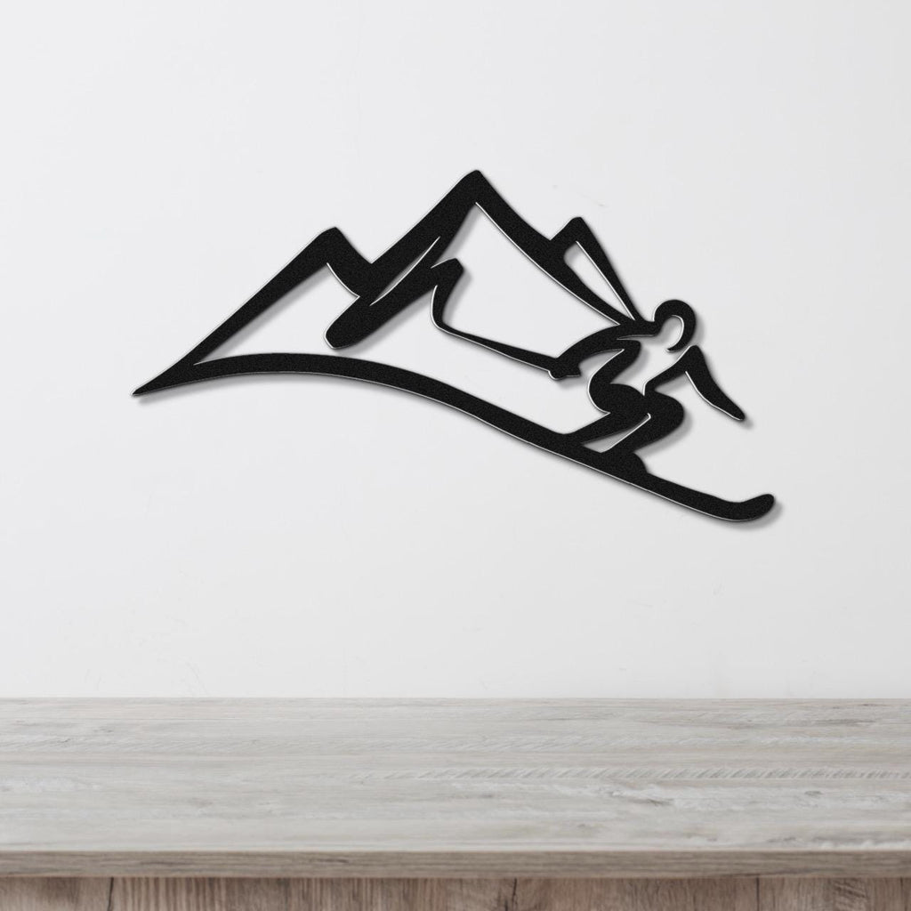 Black metal wall art featuring a skier silhouette in motion against a mountain range, mounted on a white wall above a wooden surface.