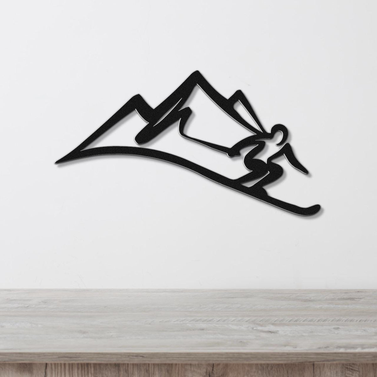 Black metal wall art featuring a skier silhouette in motion against a mountain range, mounted on a white wall above a wooden surface.