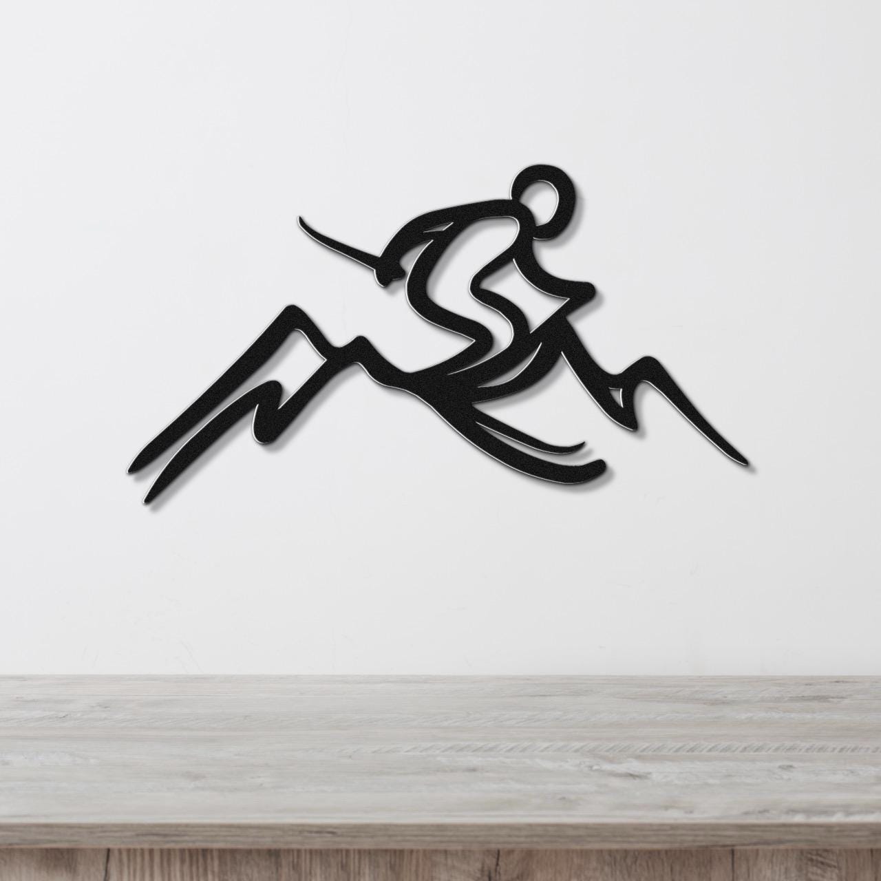 Black metal wall sculpture of a skier in motion above mountain peaks, mounted on a white wall above a light wood counter.