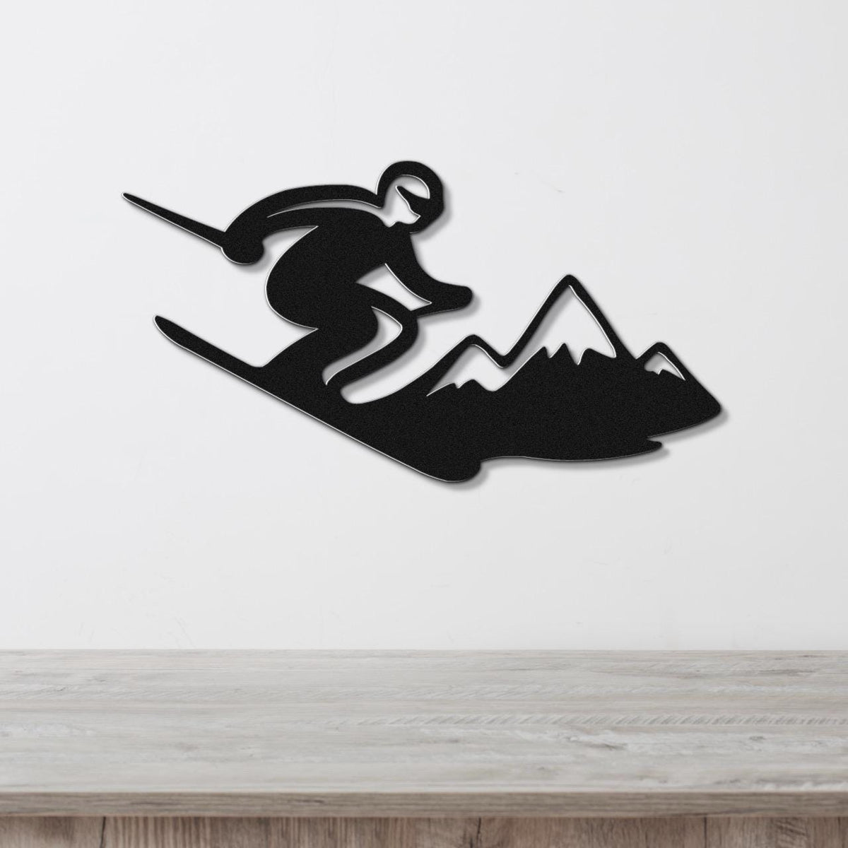 Black metal wall art silhouette of a skier in motion above a mountain range, mounted on a white wall above a wooden counter.