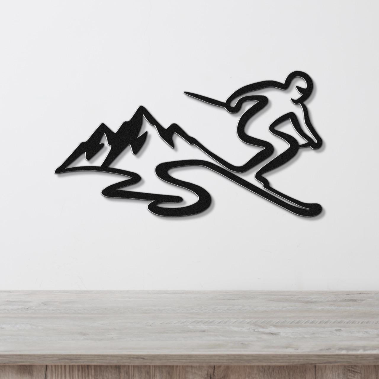 Black metal wall art cutout of a skier and mountain silhouette, mounted on a white wall above a wooden surface.