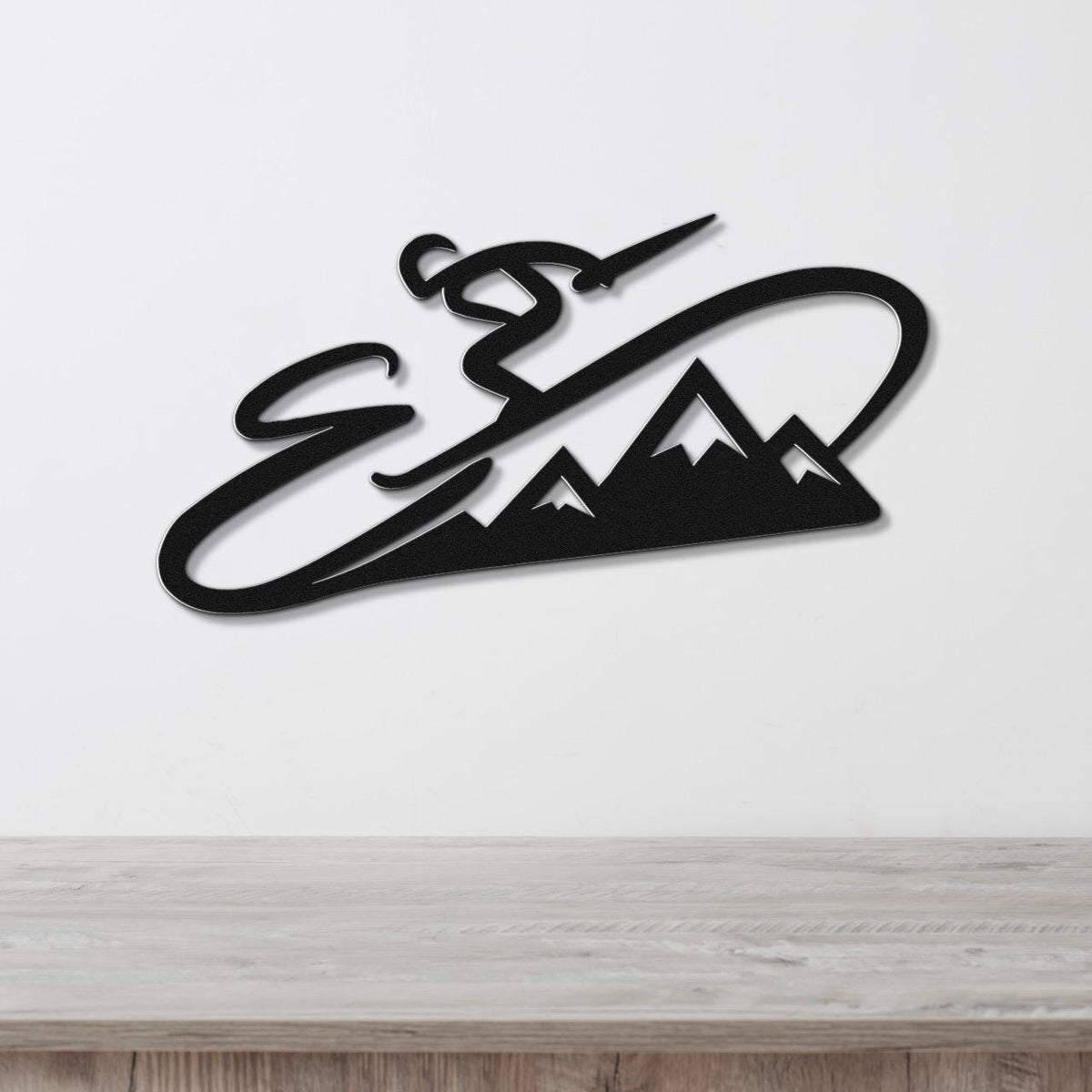 Black metal wall art featuring a skier in motion above a mountain silhouette, mounted on a white wall above a wooden surface.