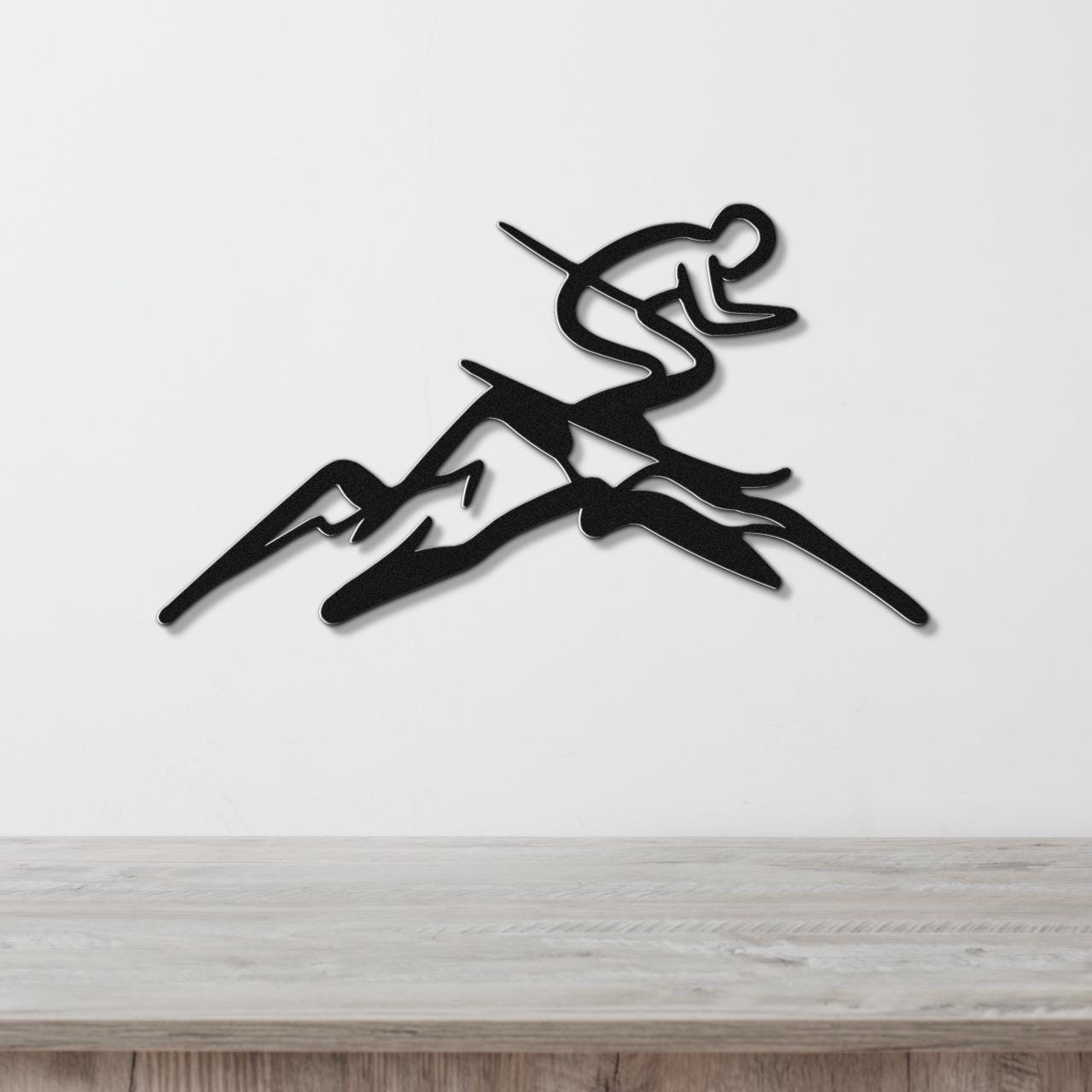 Black metal wall art featuring a skier silhouette in motion above mountain peaks, mounted on a white wall above a wooden surface.
