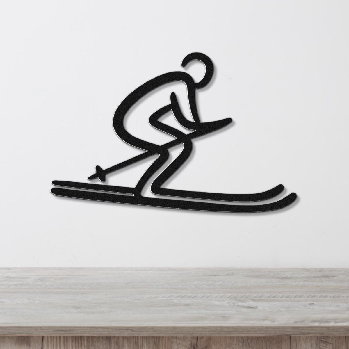 Black metal wall art of a dynamic skier silhouette with cutout details, mounted on a white wall above a light wood surface.