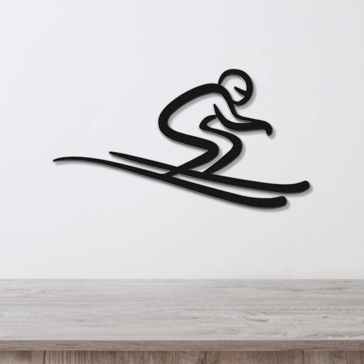 Black metal wall art featuring a minimalist skier silhouette in a crouched pose with long skis, mounted on a white wall above a wooden surface.