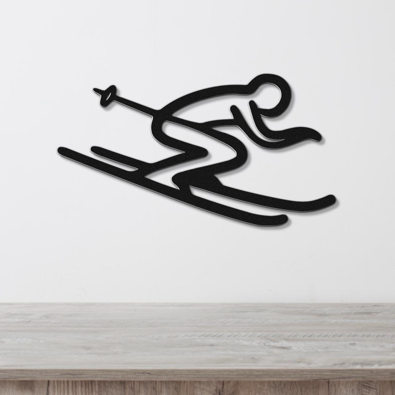 Black metal wall art in a minimalist skiing silhouette design with motion lines, mounted on a white wall above a light wood counter.