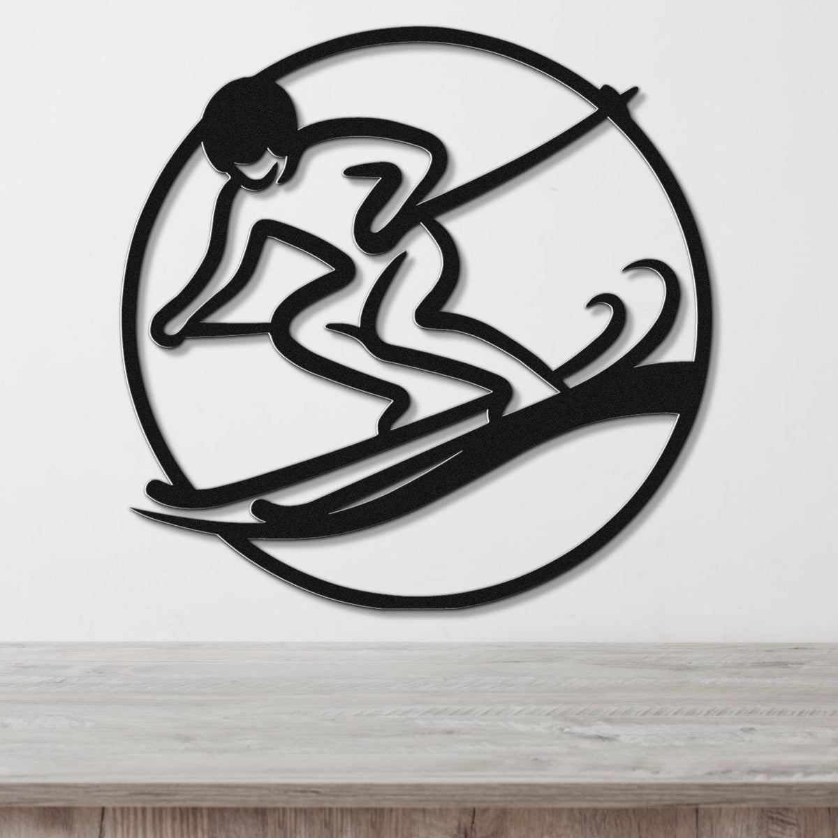 Black metal wall art featuring a skier silhouette in a circular frame with motion lines, mounted on a white wall above a wooden surface.