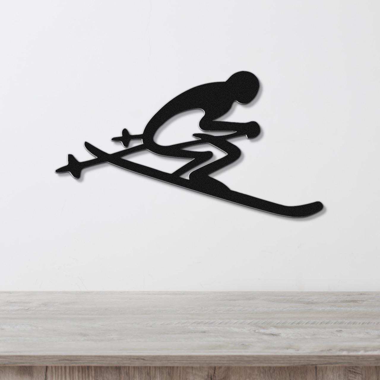 Black metal wall art of a skier silhouette with ski poles and skis, mounted on a white wall above a wooden surface.