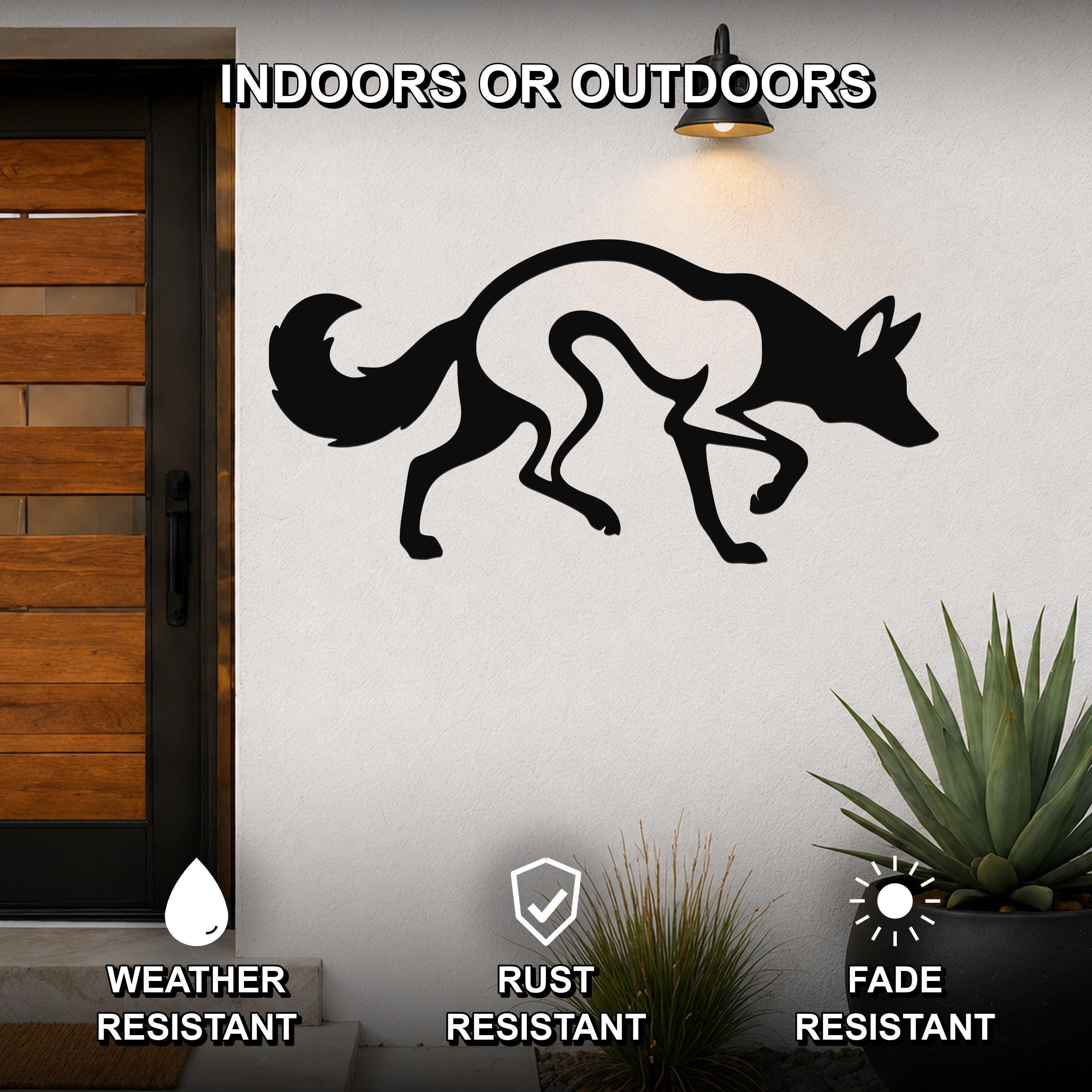 Black metal coyote wall art silhouette with internal cutout details, mounted on an outdoor wall beside a wooden door and potted plants.