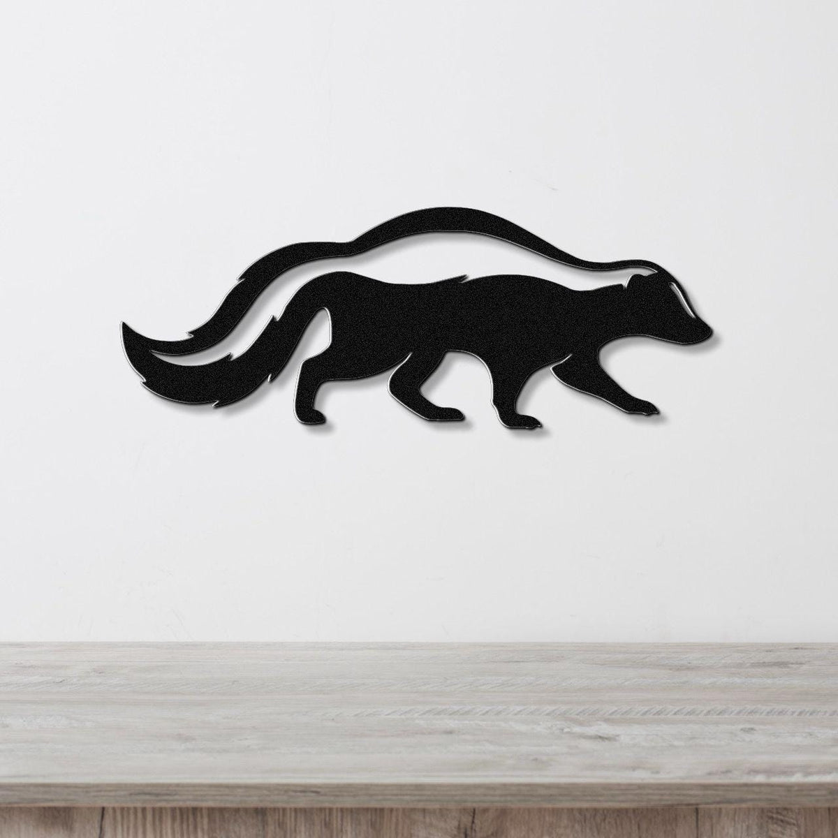 Black metal skunk wall art silhouette with a long curved tail, mounted on a white wall above a light wood surface.