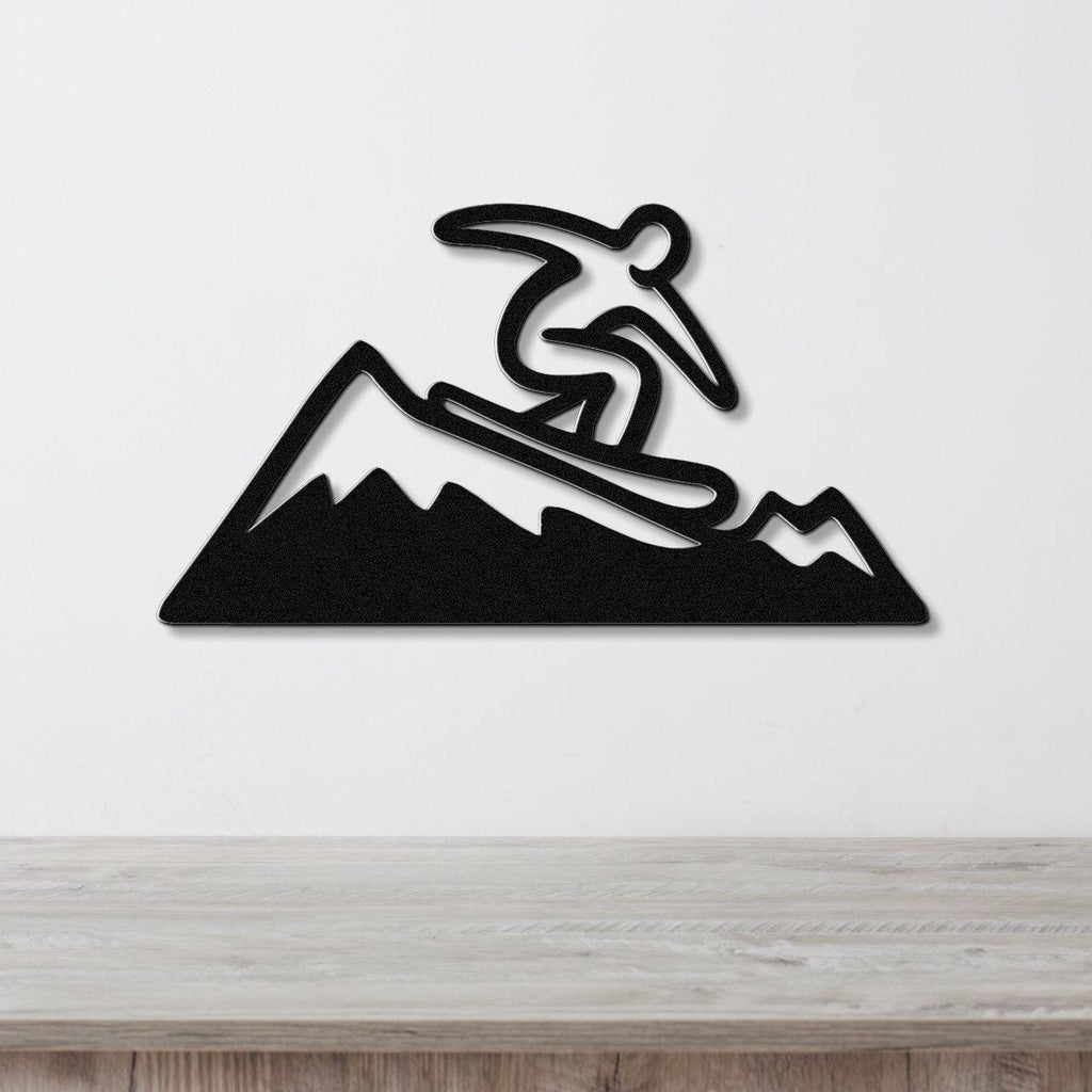 Black metal wall art featuring a snowboarder silhouette in dynamic motion above a mountain range, mounted on a white wall above a wooden counter.