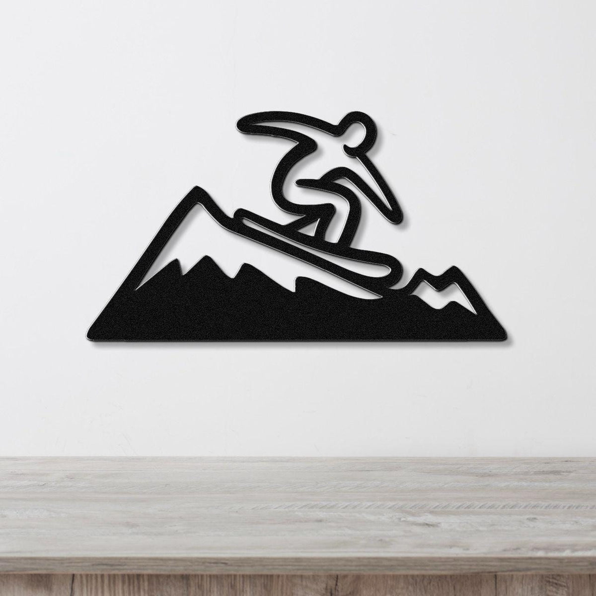 Black metal wall art featuring a snowboarder silhouette in dynamic motion above a mountain range, mounted on a white wall above a wooden counter.