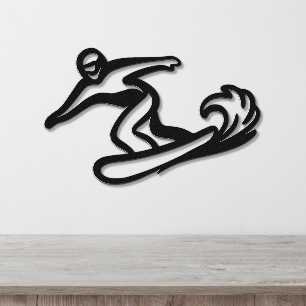 Black metal wall art silhouette of a snowboarder in motion with wave-like cutout detail, mounted on a white wall above a wooden surface.
