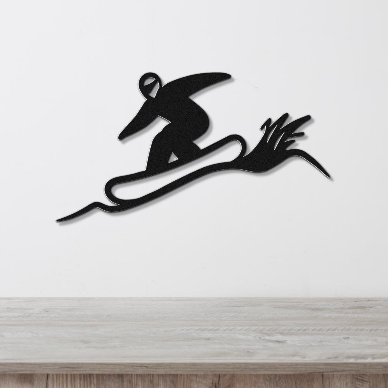 Black metal wall sculpture of a snowboarder in motion, with dynamic cutout lines, mounted on a white wall above a wooden counter.
