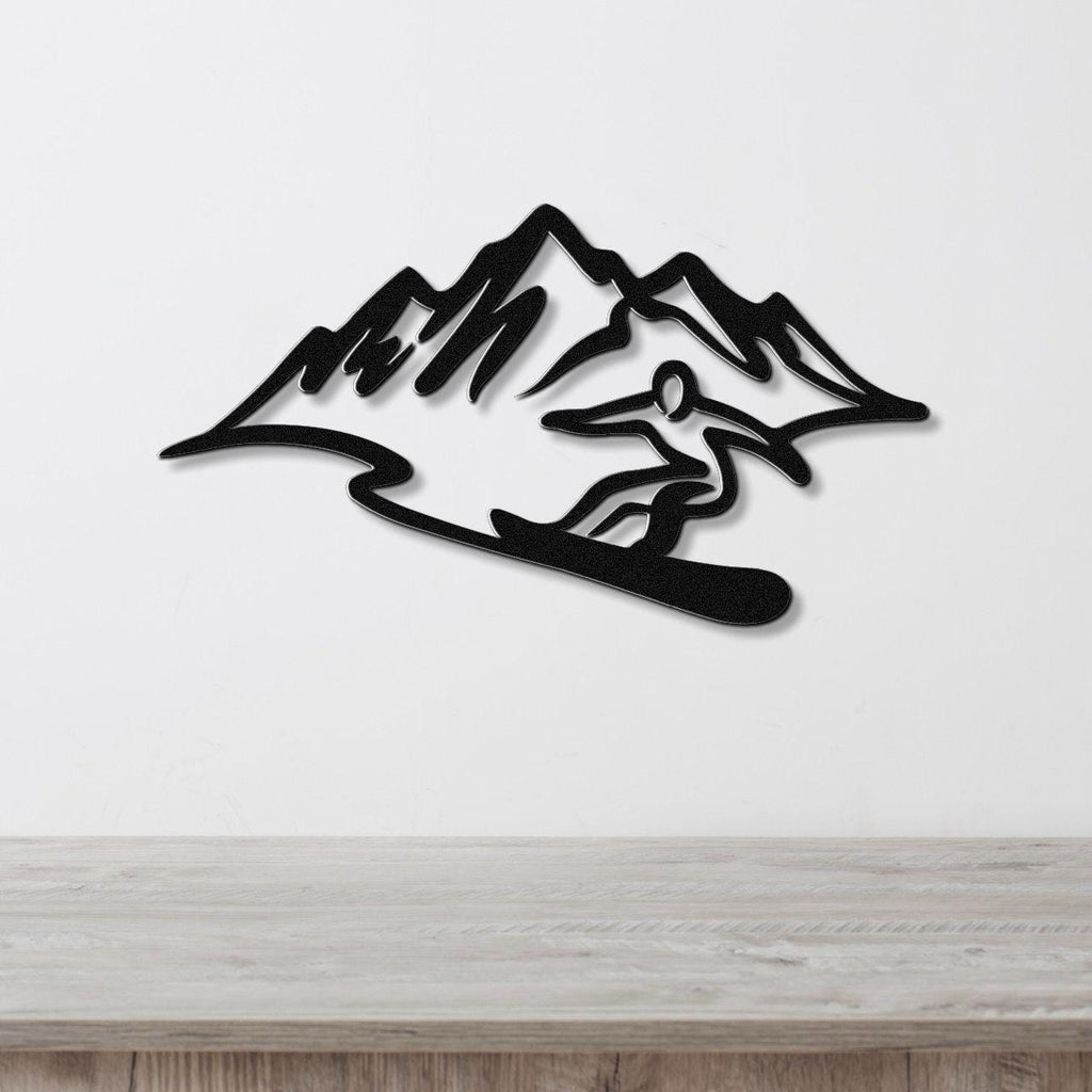 Black metal wall sculpture of a snowboarder in silhouette against mountain peaks, mounted on a white wall above a light wood counter.