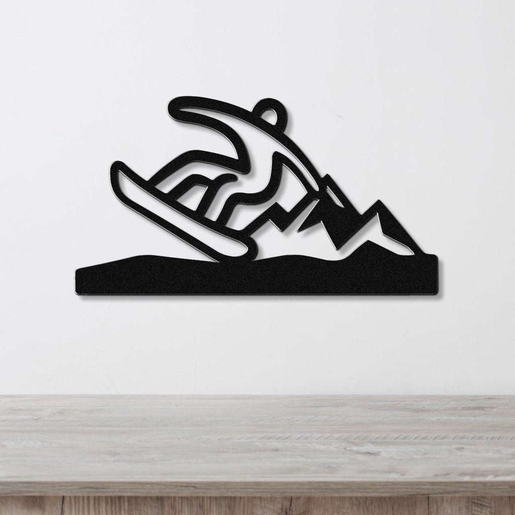 Black metal wall sculpture of a snowboarder in motion, with cutout details of mountains and snow, mounted on a white wall above a wooden surface.