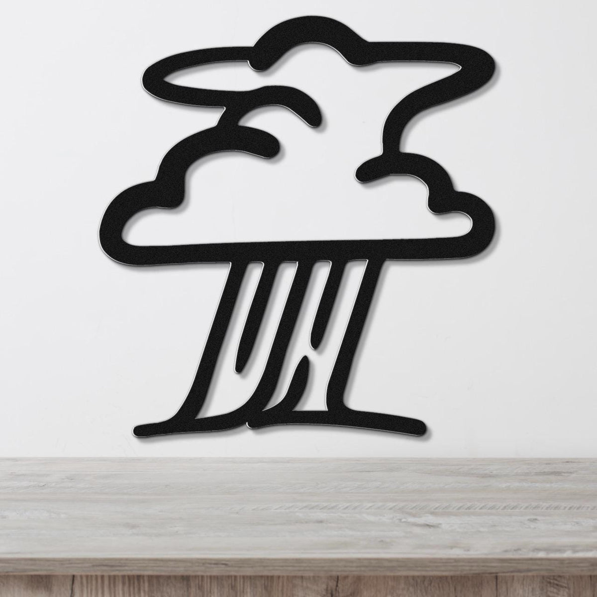 Black metal wall art in a storm cloud silhouette with raindrop cutouts, mounted on a white wall above a light wood surface.