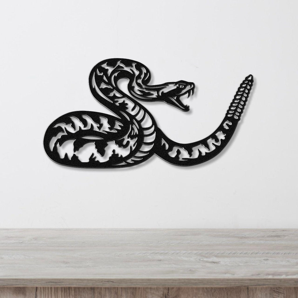 Black metal wall art of a coiled rattlesnake with intricate internal cutouts, mounted on a white wall above a light wood counter.