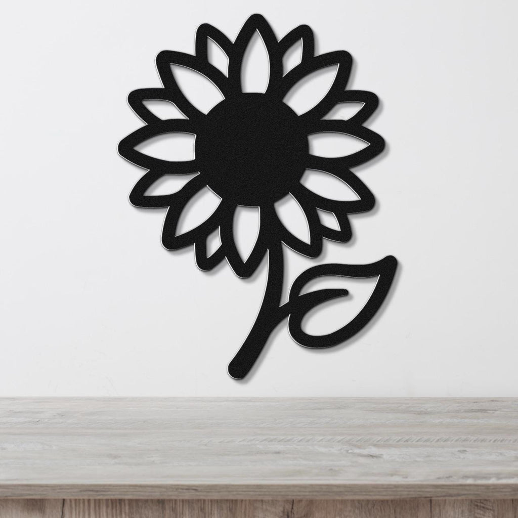 Black metal sunflower wall art with a bold silhouette and cutout petals, mounted on a white wall above a light wood countertop.