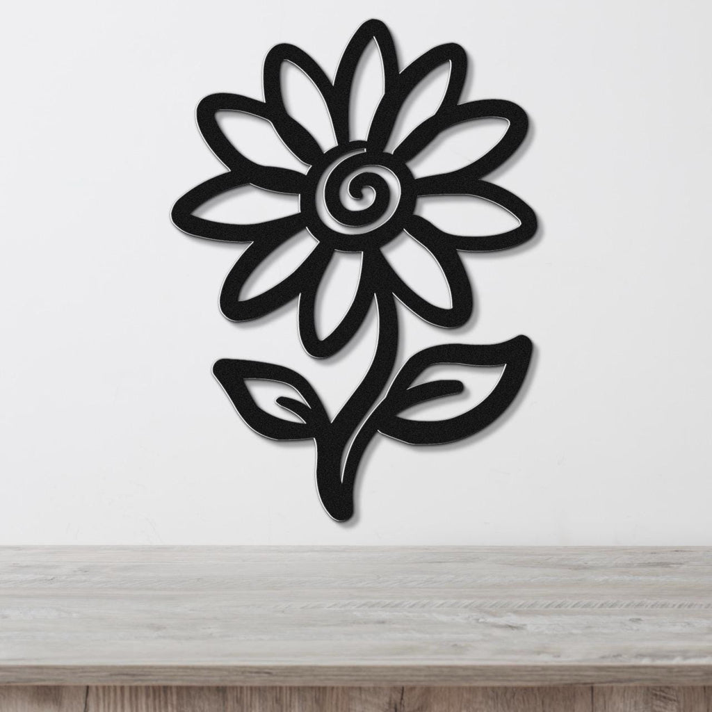 Black metal sunflower wall art with a spiral center and leaf cutouts, mounted on a white wall above a light wood surface.