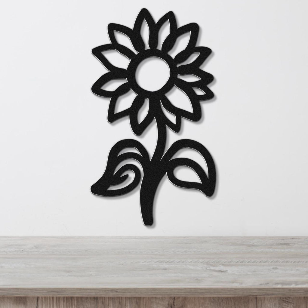 Black metal sunflower wall art with a cutout silhouette design, mounted on a white wall above a wooden surface.