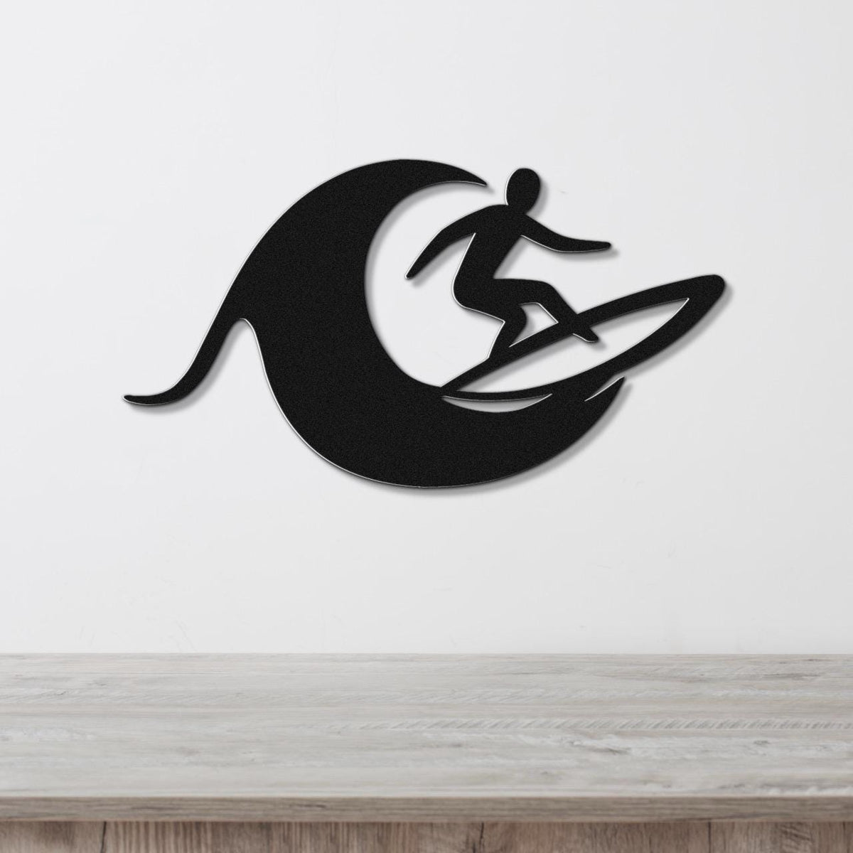 Black metal wall art featuring a surfer silhouette riding a wave, mounted on a white wall above a wooden surface.