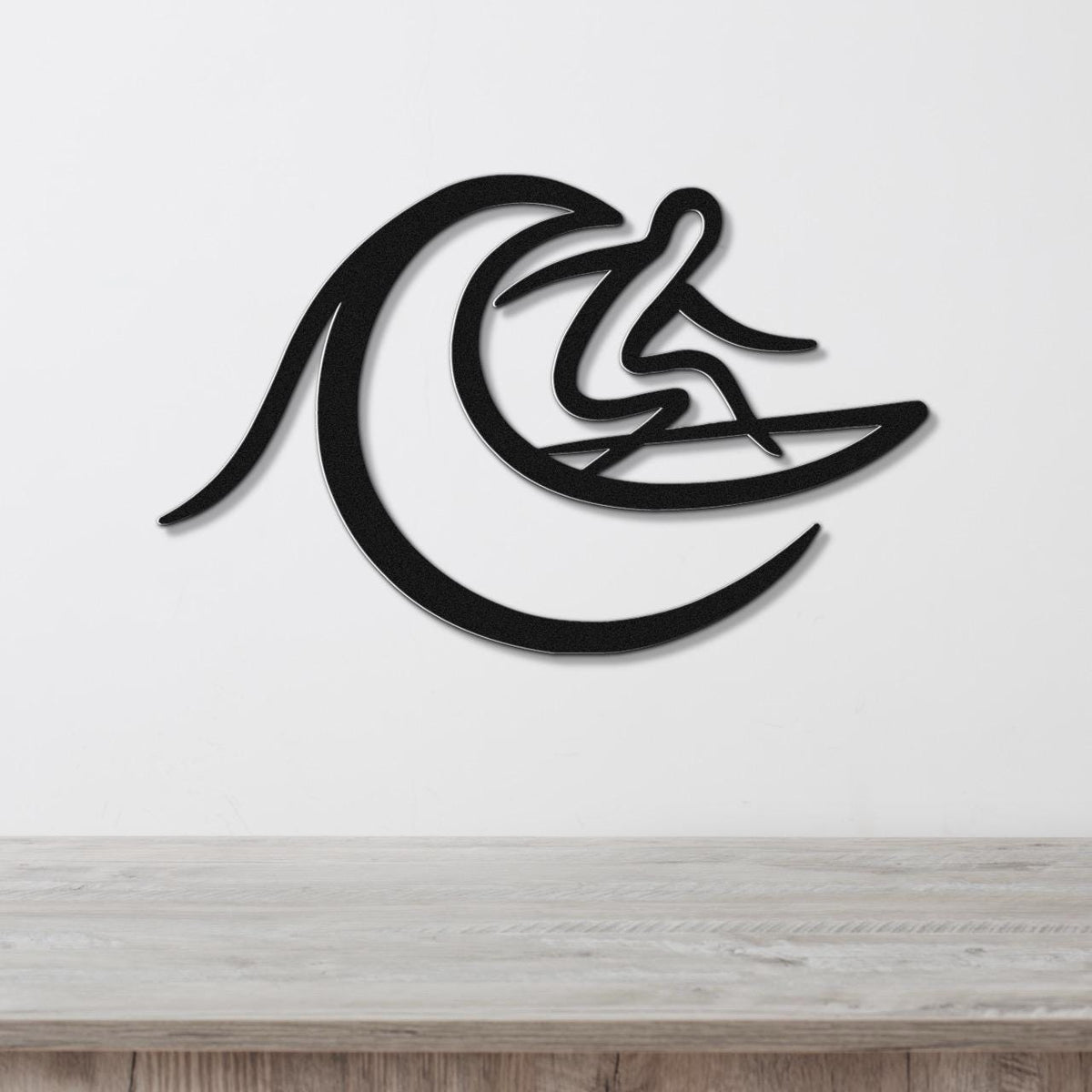 Black metal wall art featuring a surfer silhouette riding a wave, mounted on a white wall above a light wood surface.