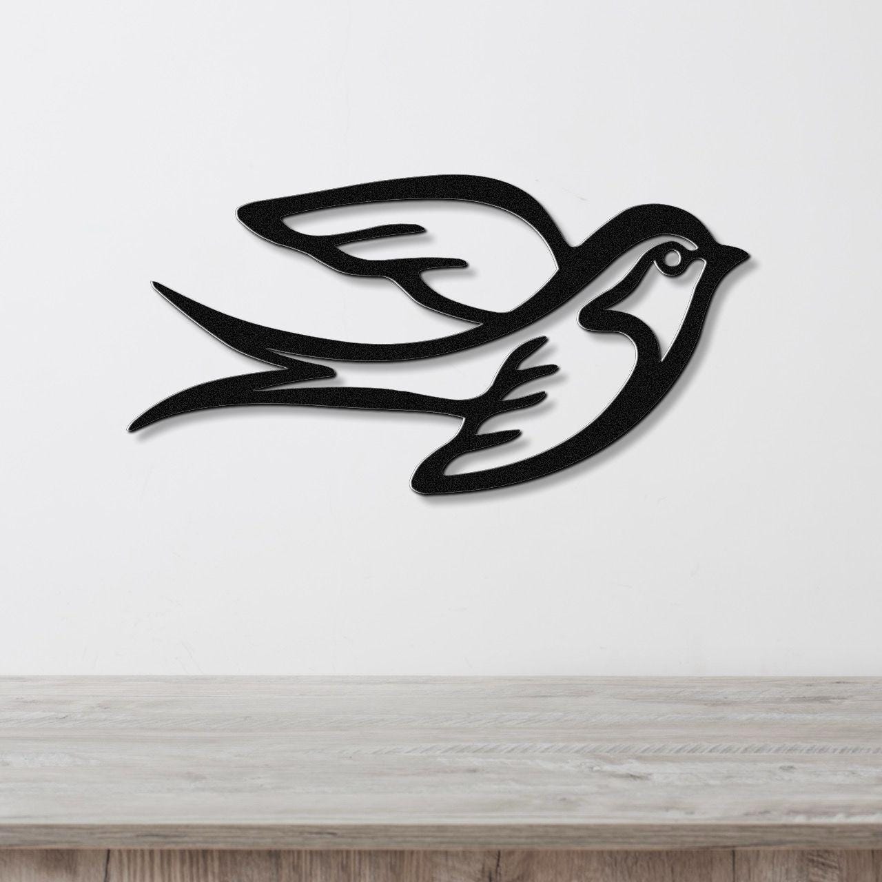 Black metal swallow bird wall art with a cutout silhouette design, mounted on a white wall above a light wood surface.