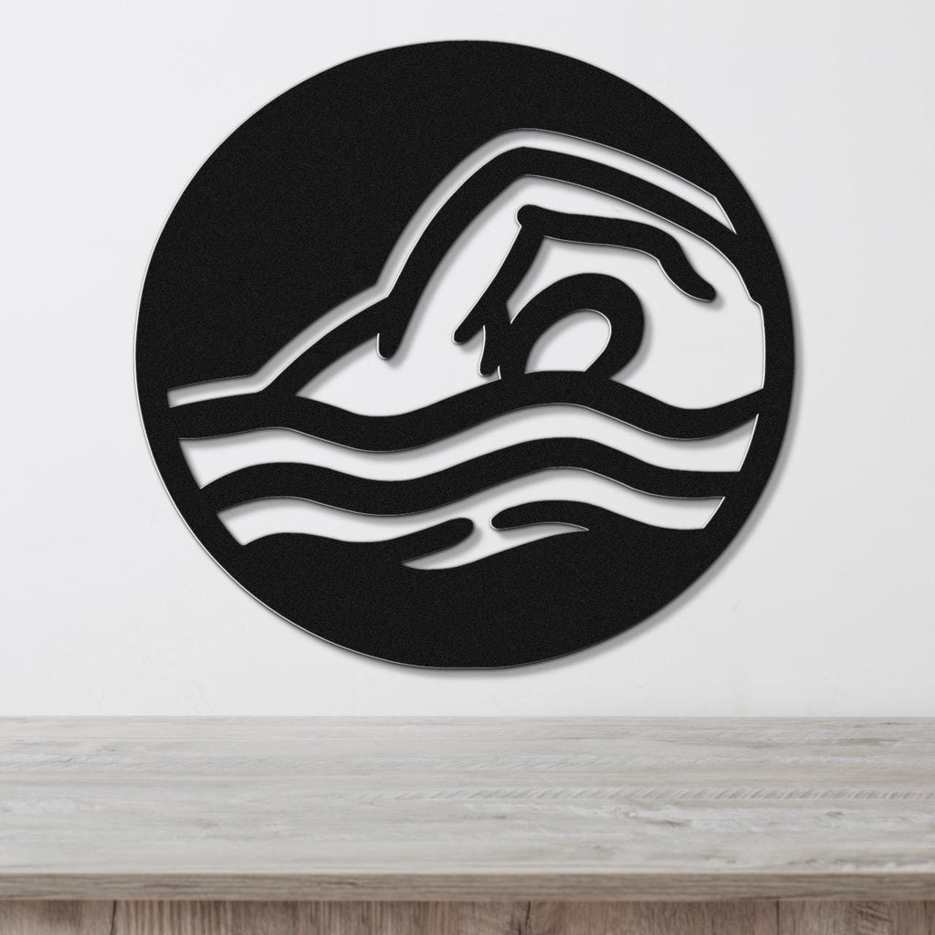 Black metal wall art with a swimmer silhouette and wavy water cutouts, mounted on a white wall above a wooden surface.