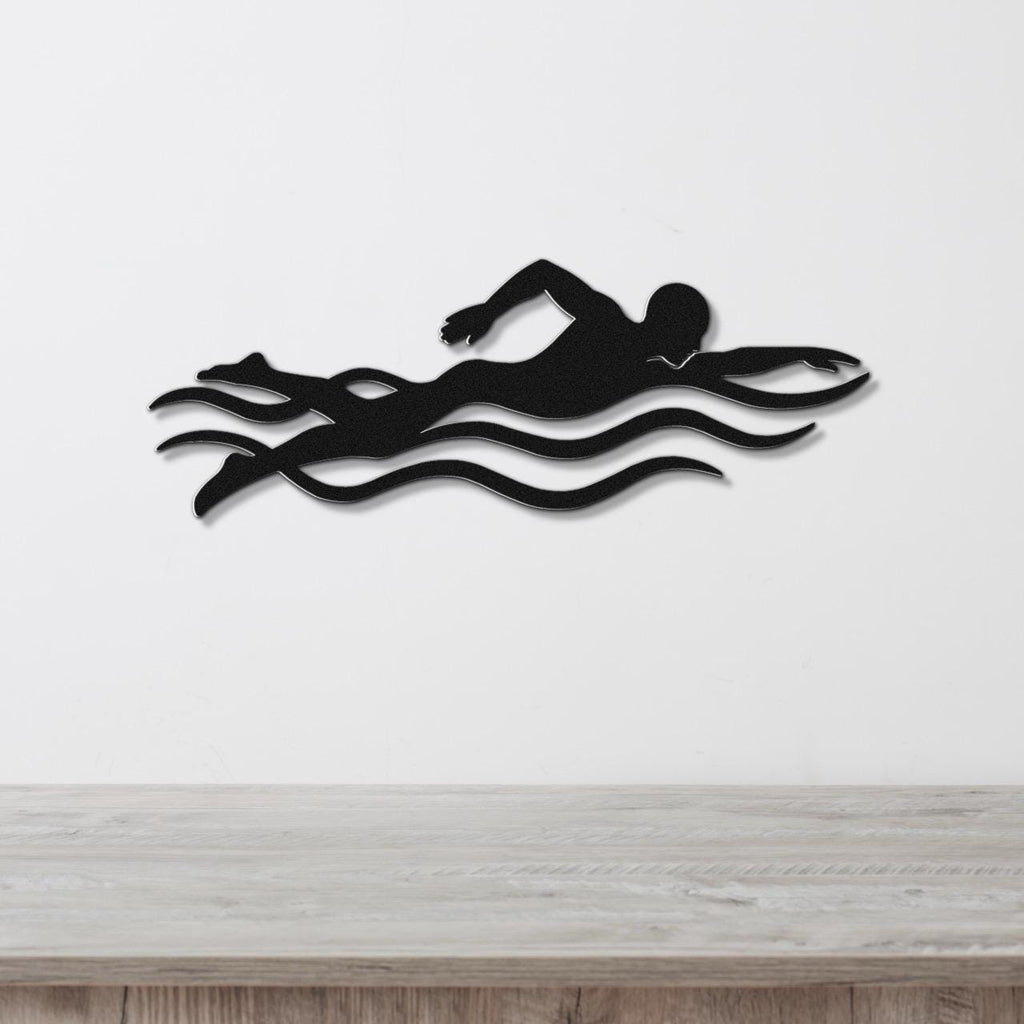 Black metal swimmer wall art with motion-line cutouts, mounted on a white wall above a wooden surface.