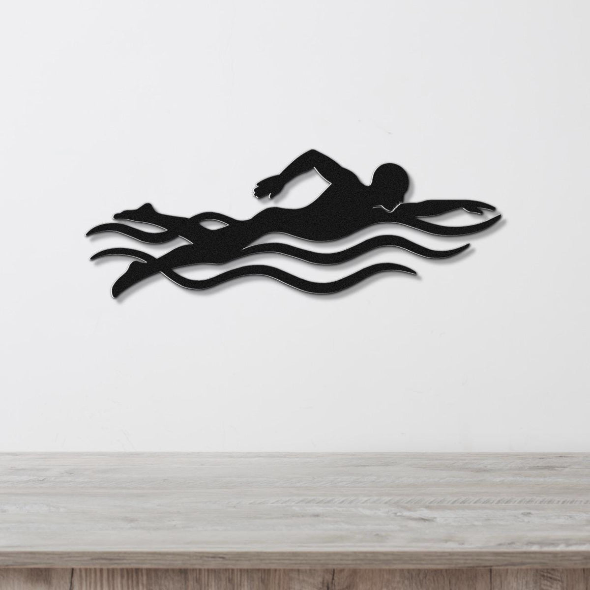 Black metal swimmer wall art with motion-line cutouts, mounted on a white wall above a wooden surface.