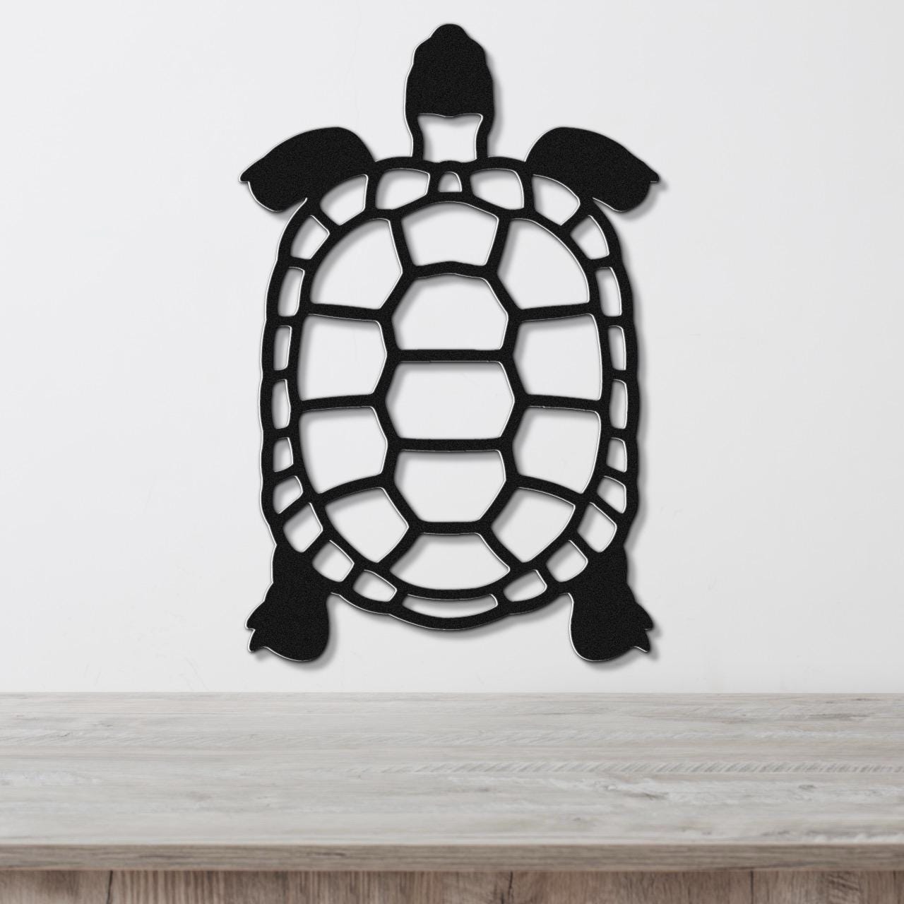 Black metal turtle wall art with a cutout shell design, mounted on a white wall above a light wood surface.