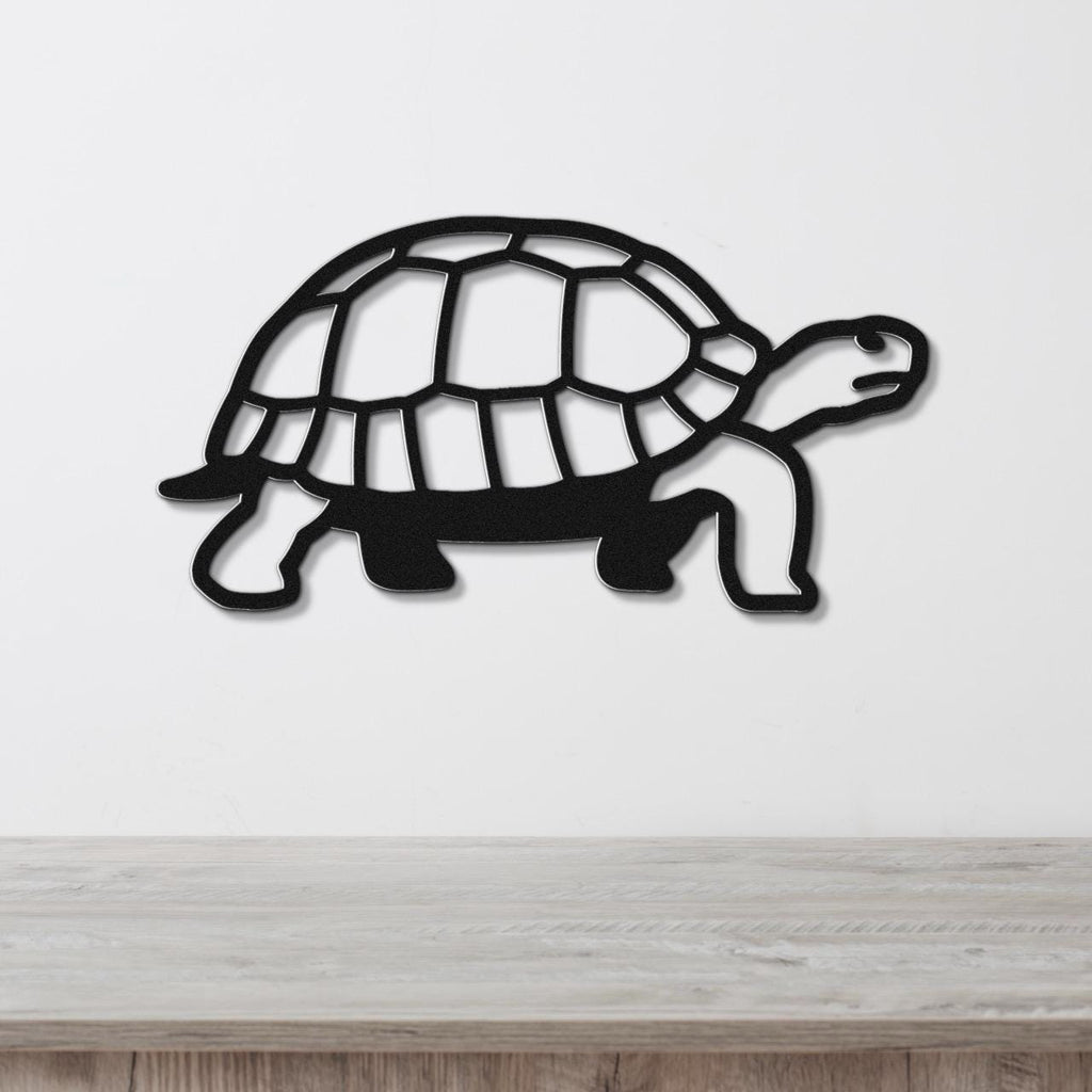 Black metal tortoise wall art with a cutout shell pattern, mounted on a white wall above a light wood surface.