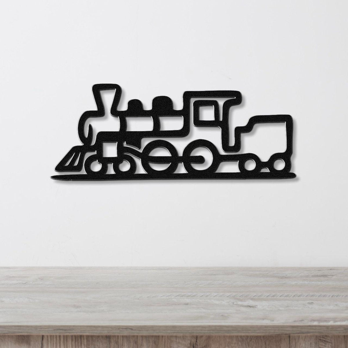 Black metal train wall art with a bold silhouette design and internal cutouts, mounted on a white wall above a light wood surface.