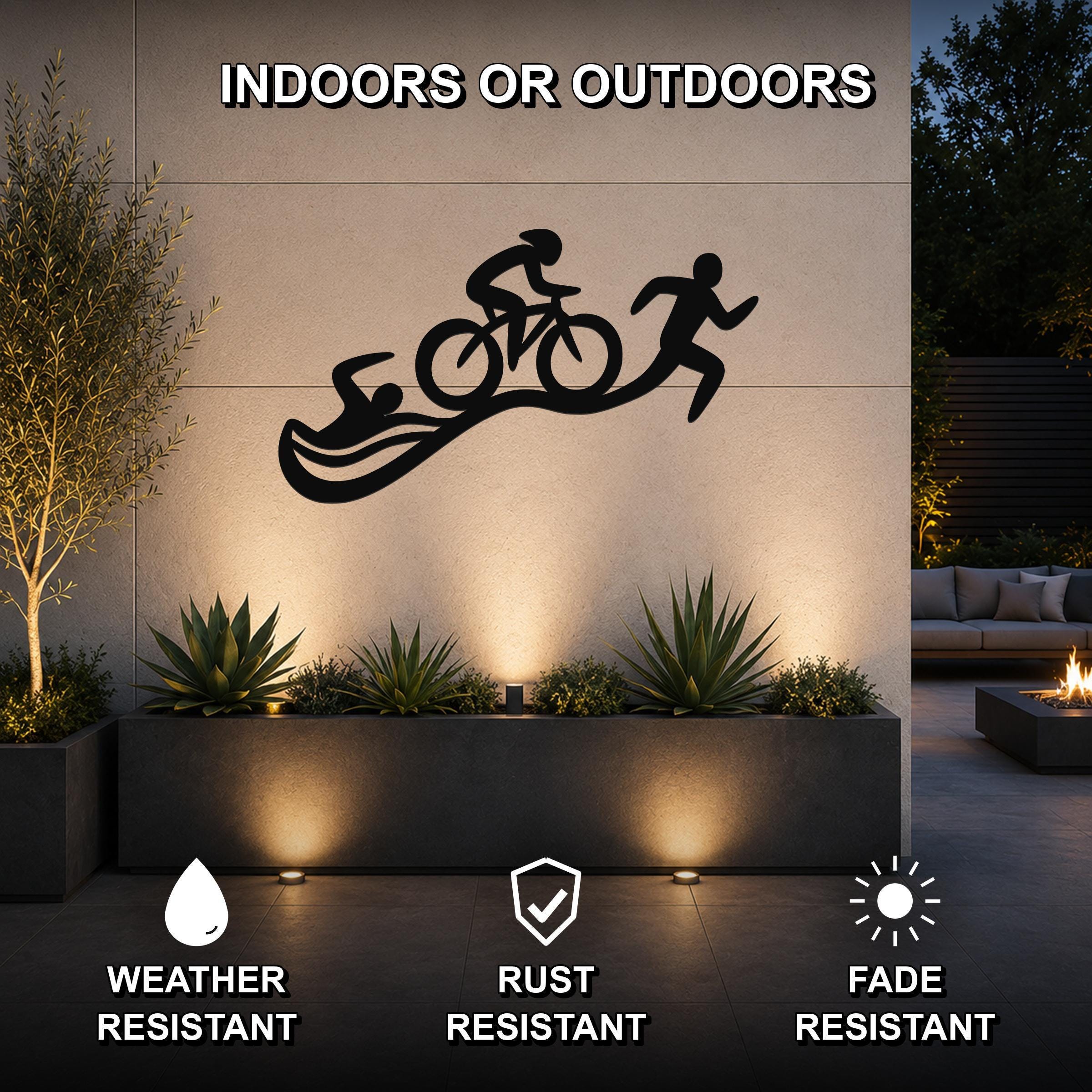 Black metal triathlon wall art with swim, bike, and run silhouettes, mounted on an outdoor wall above a planter in a modern patio setting.
