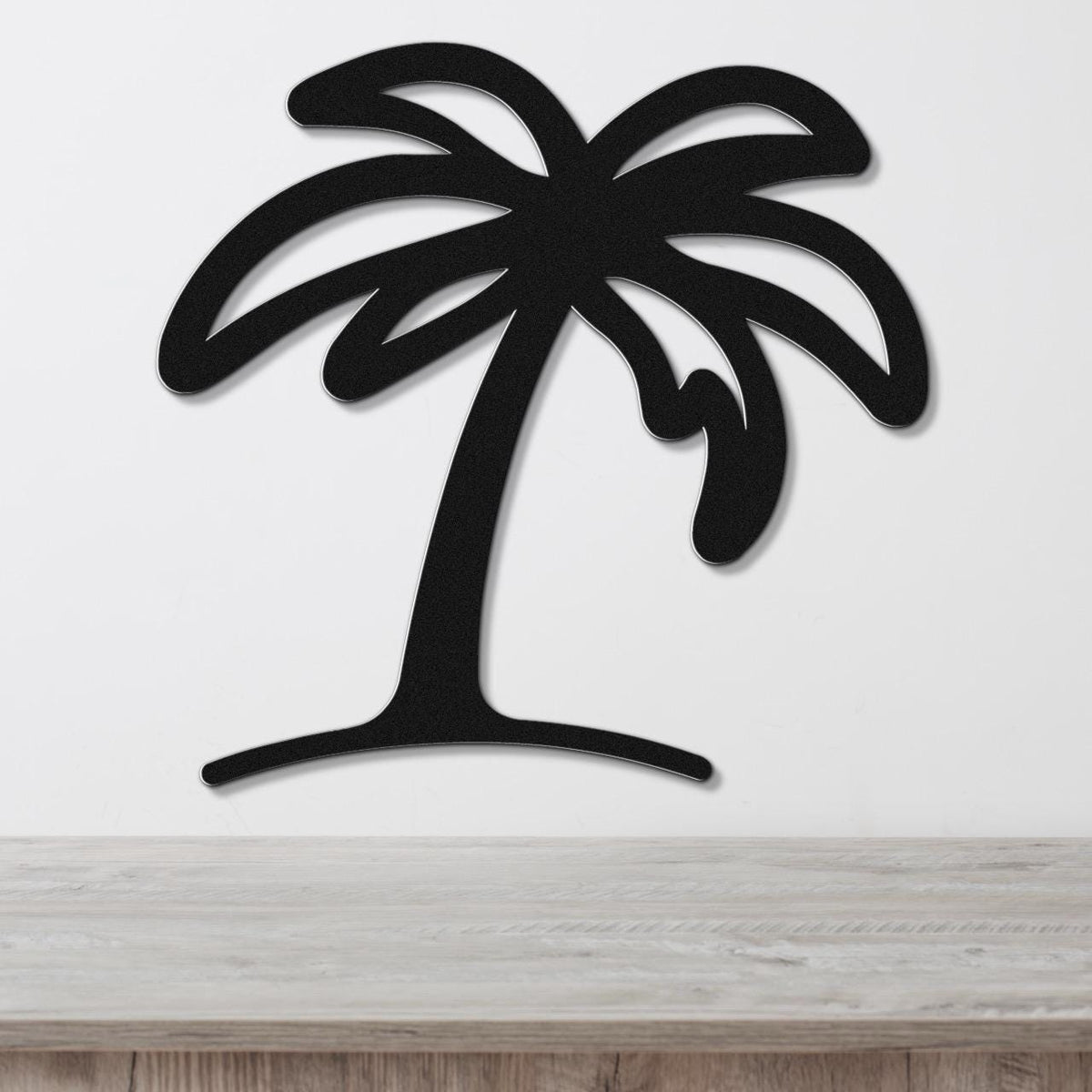 Black metal palm tree wall art with leaf cutouts, mounted on a white wall above a light wood surface.