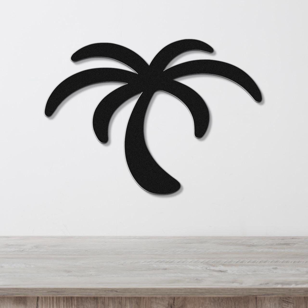 Black metal palm tree wall art with a silhouette design, mounted on a white wall above a light wood surface.