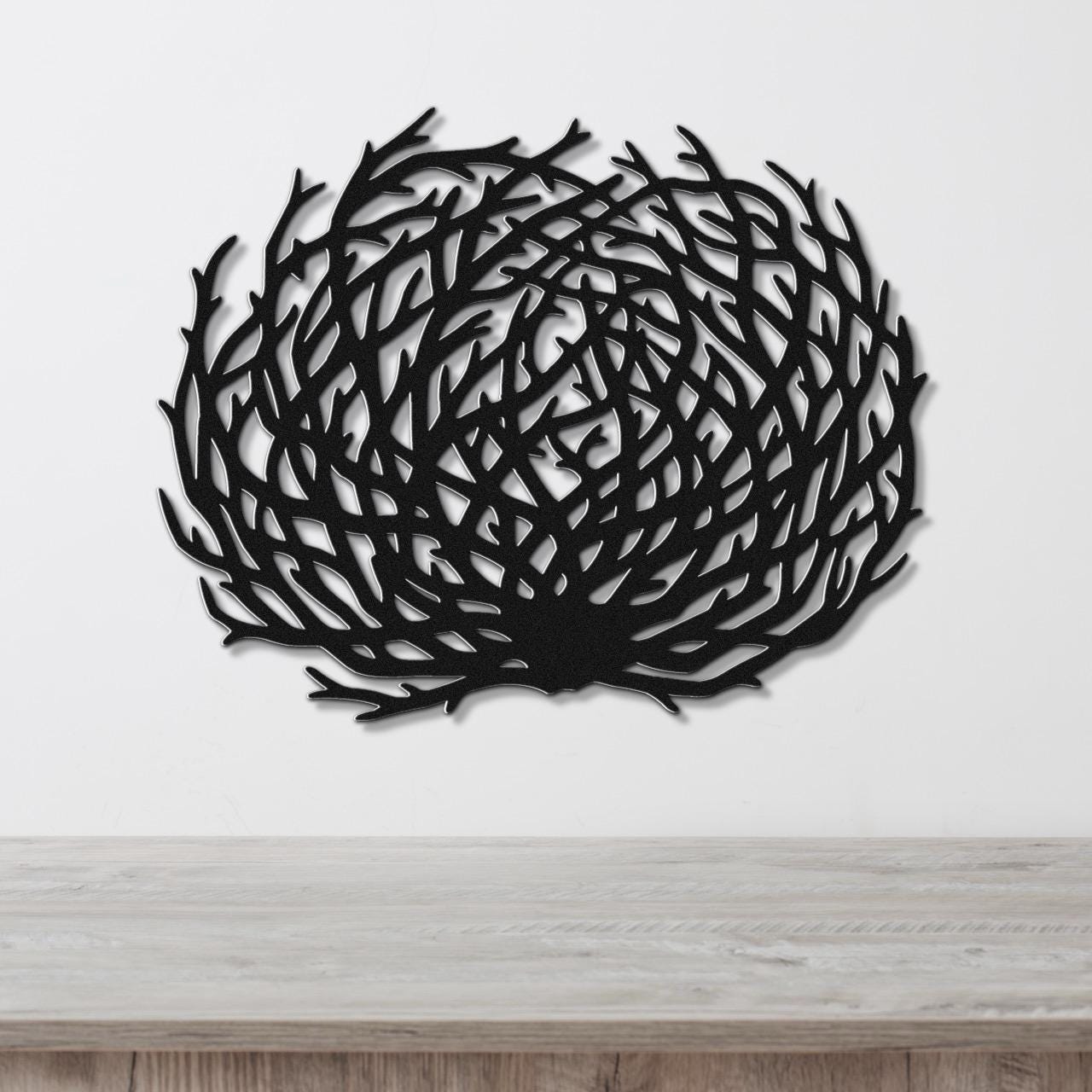 Black metal wall art in a circular tumbleweed silhouette with intricate branch cutouts, mounted on a white wall above a light wood counter.