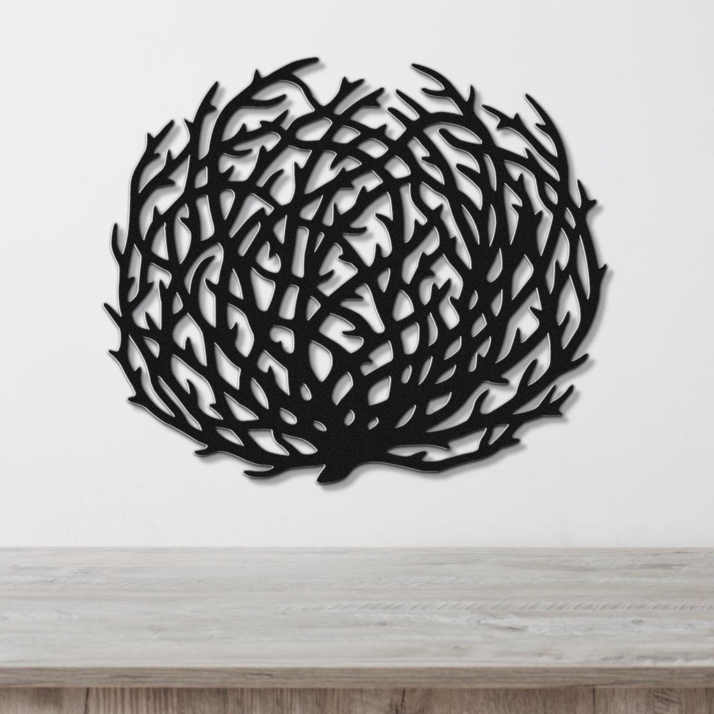 Black metal tumbleweed wall art with intricate branch cutouts, mounted on a white wall above a light wood counter.